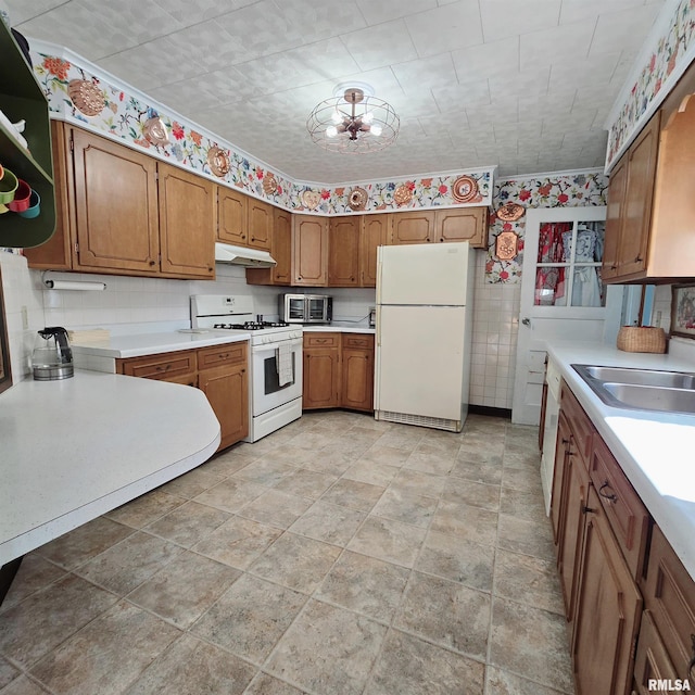 kitchen featuring brown cabinets, light countertops, a sink, white appliances, and under cabinet range hood