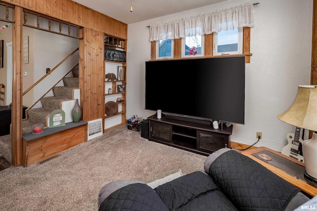 living area featuring stairway, carpet, visible vents, and wooden walls