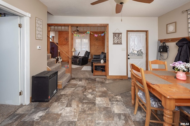 dining space featuring stone finish floor, ceiling fan, and stairway