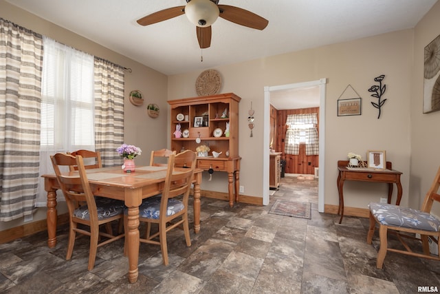 dining room featuring stone finish flooring, a ceiling fan, and baseboards