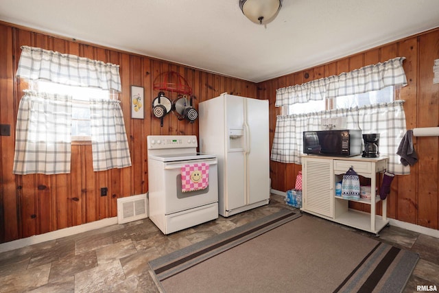 kitchen with white appliances, wooden walls, and visible vents