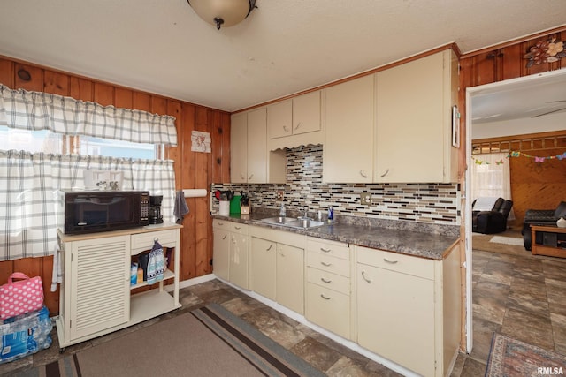 kitchen with dark countertops, backsplash, stone finish floor, a sink, and black microwave