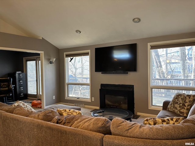 carpeted living room with a glass covered fireplace, visible vents, vaulted ceiling, and baseboards