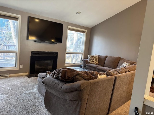 living area featuring vaulted ceiling, carpet floors, a fireplace with flush hearth, and a wealth of natural light