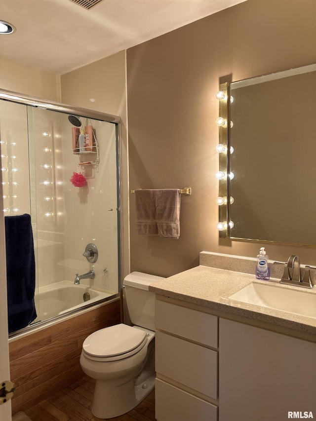 bathroom with wood finished floors, vanity, toilet, and bath / shower combo with glass door