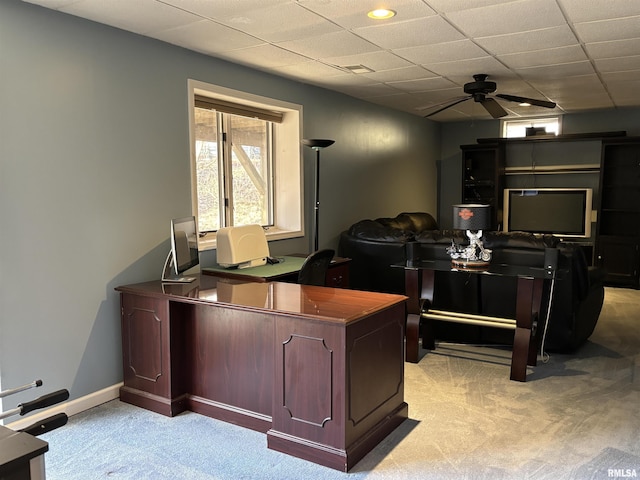 home office featuring ceiling fan, a drop ceiling, baseboards, and light colored carpet