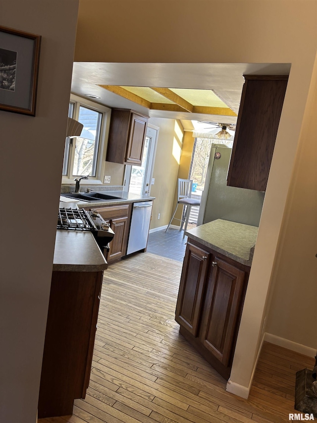 kitchen featuring appliances with stainless steel finishes, a sink, ceiling fan, light wood-type flooring, and baseboards