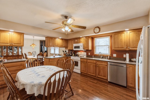 kitchen with ceiling fan, white appliances, dark wood-type flooring, a sink, and brown cabinets