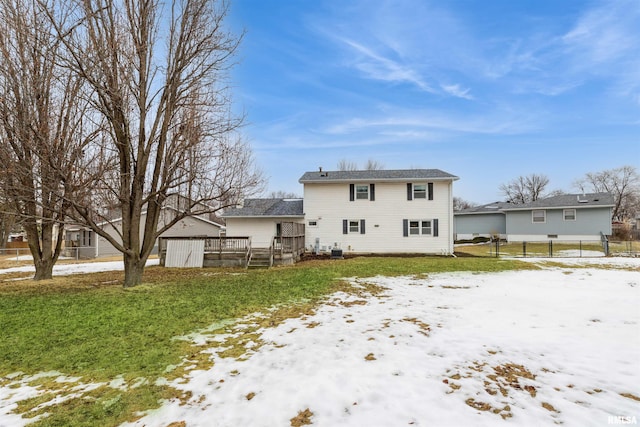 snow covered rear of property featuring a yard, fence, a deck, and an outdoor structure