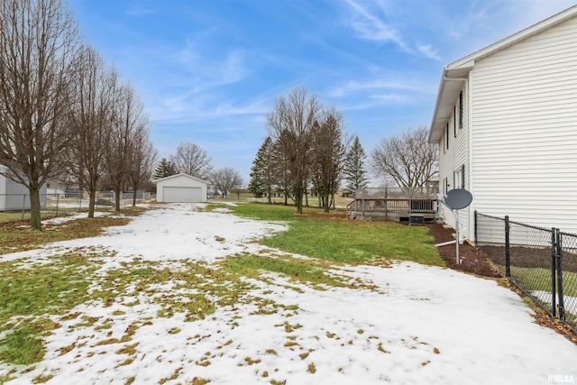 yard covered in snow with a wooden deck, a detached garage, fence, and an outdoor structure