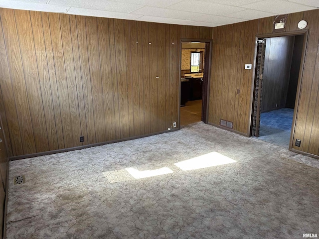 carpeted empty room featuring visible vents, wooden walls, and baseboards