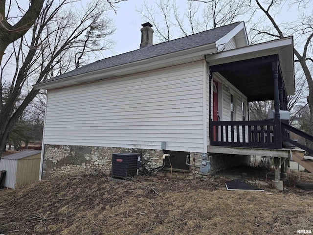 view of property exterior with a porch, a storage shed, central AC, an outdoor structure, and a chimney