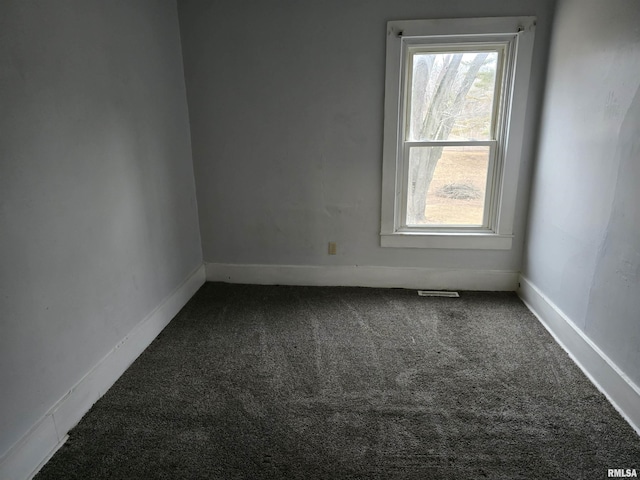 empty room featuring baseboards, dark colored carpet, and a wealth of natural light