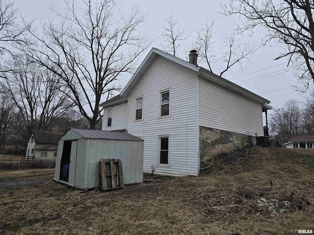 view of property exterior featuring a storage shed, a chimney, metal roof, and an outdoor structure