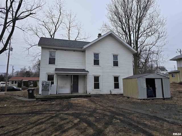 view of front facade with a storage shed, a shingled roof, a chimney, and an outdoor structure