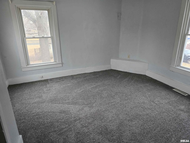 unfurnished room featuring plenty of natural light, visible vents, dark carpet, and baseboards