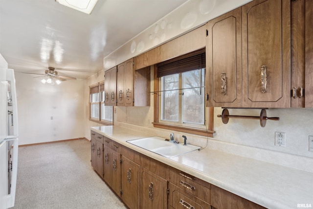 kitchen with a sink, a ceiling fan, baseboards, light countertops, and brown cabinetry