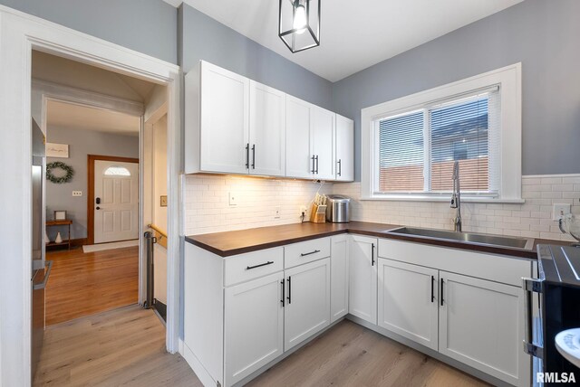 kitchen featuring light wood finished floors, backsplash, white cabinetry, a sink, and black microwave