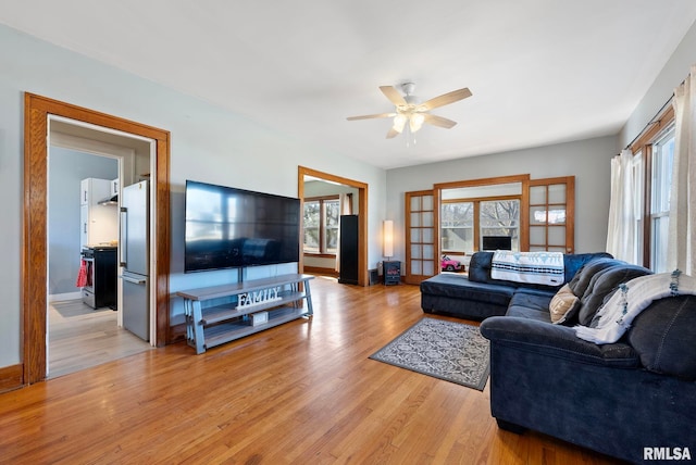 living area featuring light wood-style floors, plenty of natural light, baseboards, and ceiling fan