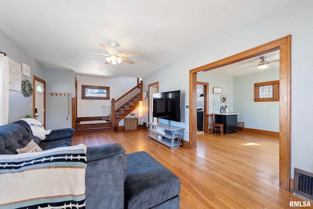 living area with ceiling fan, stairs, visible vents, and wood finished floors