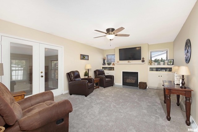 carpeted living area featuring a healthy amount of sunlight, a fireplace with flush hearth, ceiling fan, and french doors