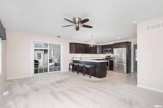 kitchen with stainless steel appliances, visible vents, a kitchen breakfast bar, dark brown cabinets, and light countertops