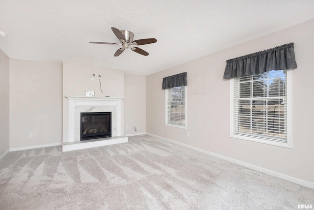 unfurnished living room with baseboards, light colored carpet, ceiling fan, a textured ceiling, and a fireplace