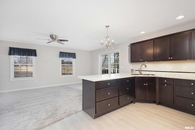 kitchen with open floor plan, a peninsula, light countertops, dark brown cabinets, and a sink