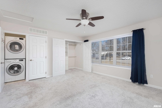 unfurnished bedroom with carpet floors, a textured ceiling, visible vents, and stacked washer / dryer