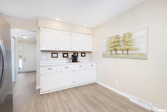 kitchen featuring light wood finished floors, light countertops, visible vents, freestanding refrigerator, and white cabinetry