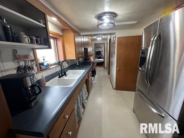 kitchen featuring a sink, stainless steel refrigerator with ice dispenser, brown cabinets, light floors, and dark countertops