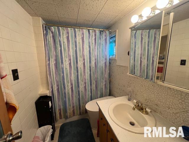 bathroom with toilet, shower / bath combo with shower curtain, tile walls, and vanity