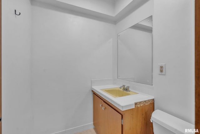 half bathroom with baseboards, vanity, and toilet