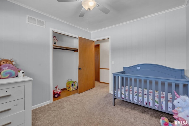 bedroom featuring ceiling fan, visible vents, ornamental molding, a crib, and carpet