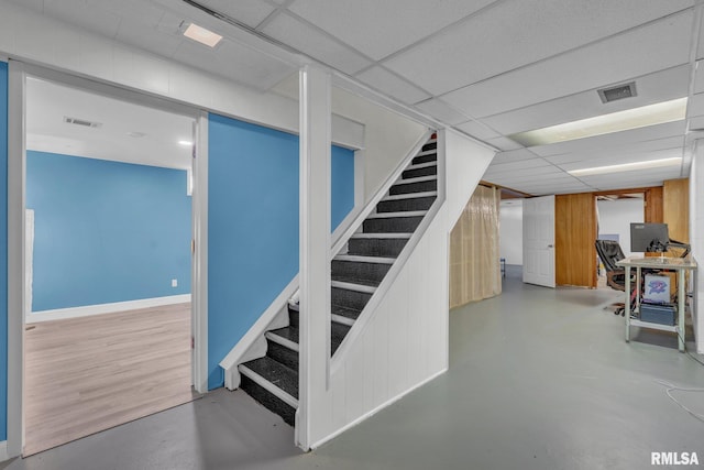 finished basement featuring baseboards, visible vents, stairway, and a drop ceiling