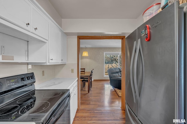 kitchen featuring electric range, tasteful backsplash, wood finished floors, freestanding refrigerator, and white cabinetry