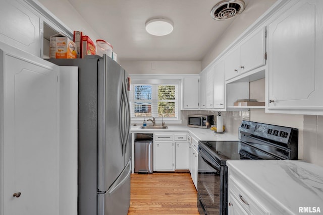 kitchen with stainless steel appliances, white cabinetry, visible vents, and light wood-style floors