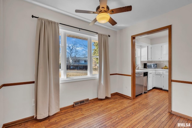 unfurnished dining area featuring light wood finished floors, a ceiling fan, visible vents, and baseboards