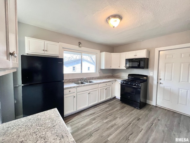 kitchen with black appliances, light wood-type flooring, a sink, and white cabinets