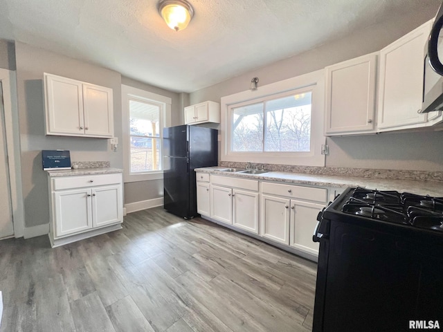 kitchen featuring a sink, black appliances, white cabinetry, and light wood-style floors