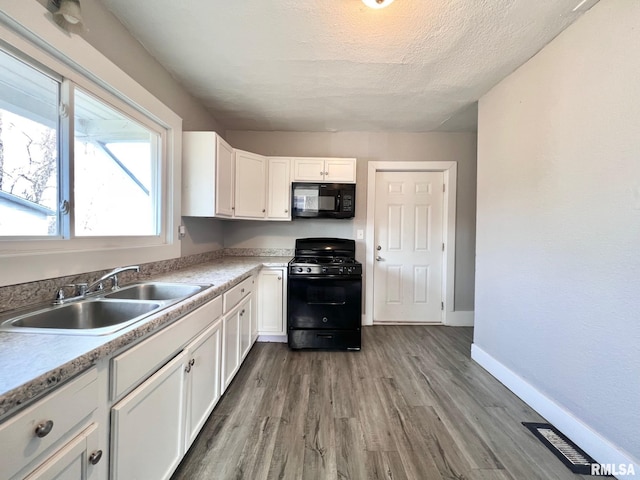 kitchen featuring black appliances, white cabinetry, a sink, and wood finished floors