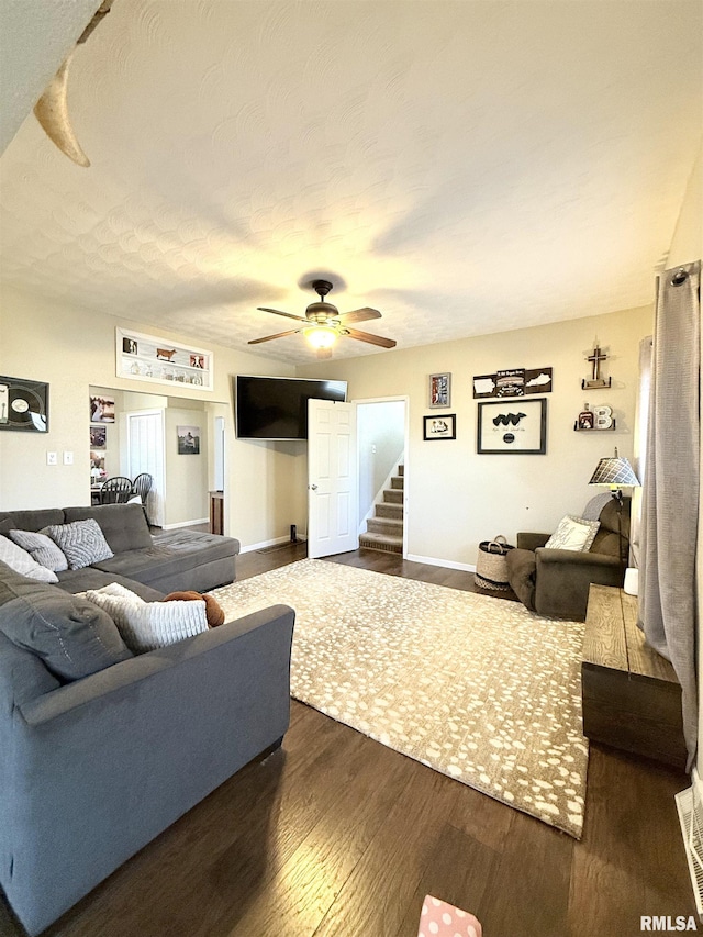 living area featuring stairway, baseboards, dark wood-style floors, and a ceiling fan