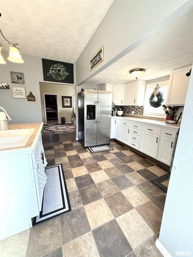 kitchen featuring a sink, tasteful backsplash, white cabinetry, stainless steel fridge with ice dispenser, and light countertops