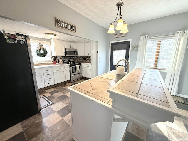 kitchen with a wealth of natural light, a sink, backsplash, white cabinetry, and appliances with stainless steel finishes