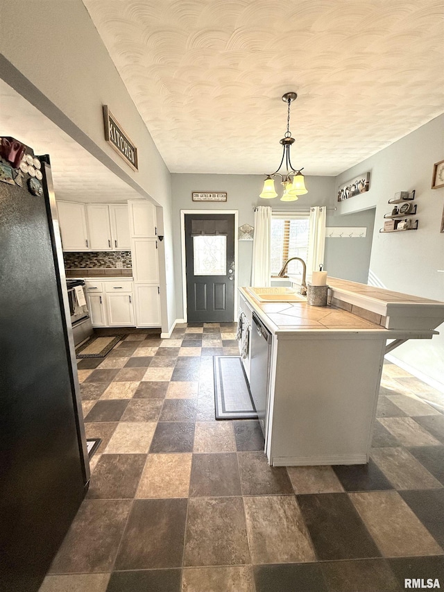 kitchen with a sink, backsplash, white cabinetry, stainless steel appliances, and tile counters