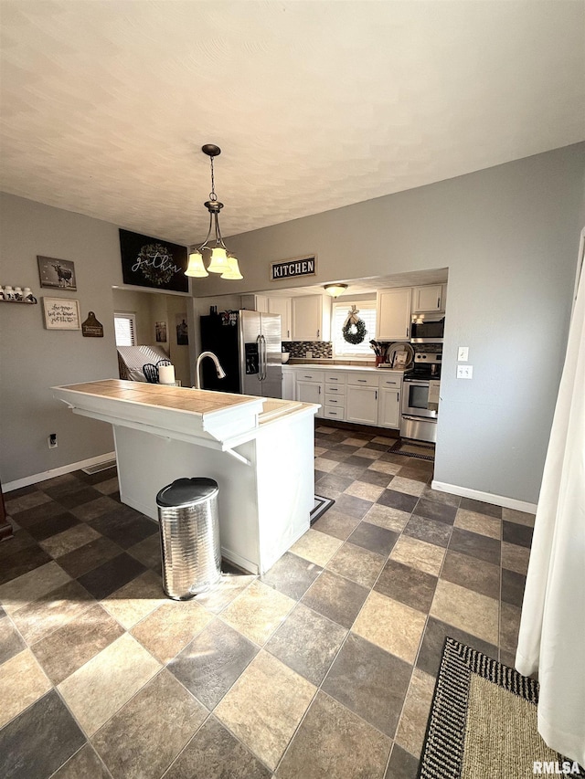 kitchen with baseboards, decorative light fixtures, light countertops, white cabinets, and stainless steel appliances