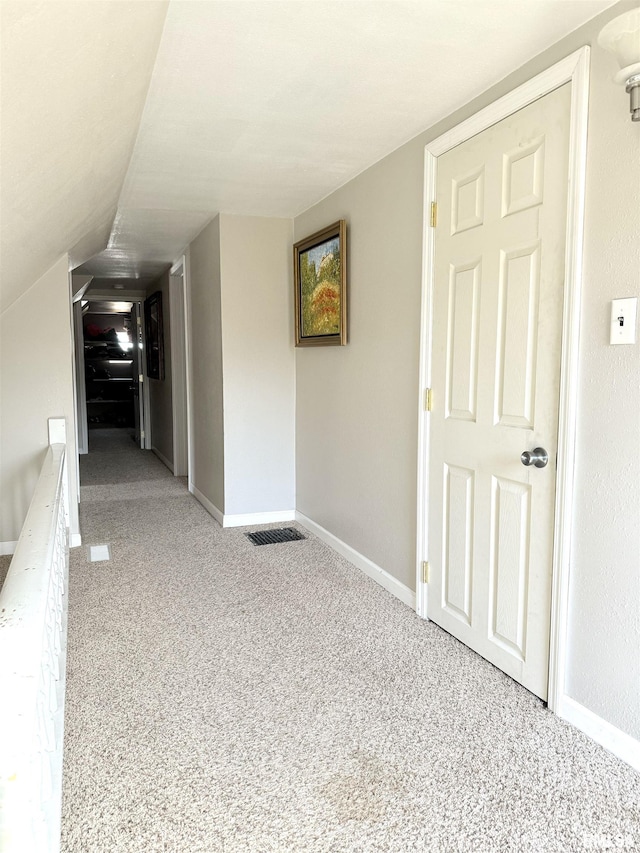 hallway featuring visible vents, baseboards, carpet, and vaulted ceiling