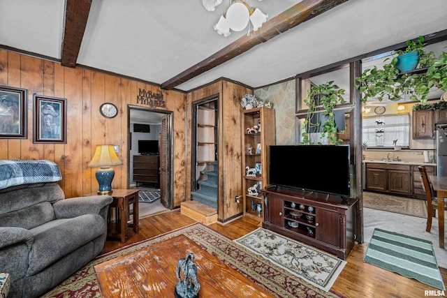 living area featuring beamed ceiling, wood walls, stairs, and light wood finished floors