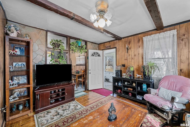 living room featuring beamed ceiling, wooden walls, wood finished floors, and ceiling fan