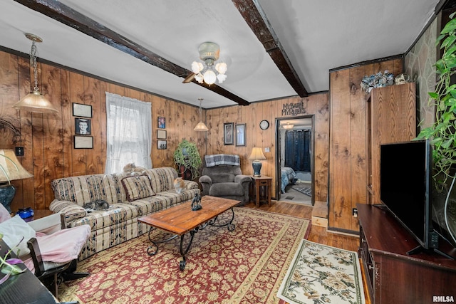 living area with beamed ceiling, wood walls, ceiling fan, and wood finished floors